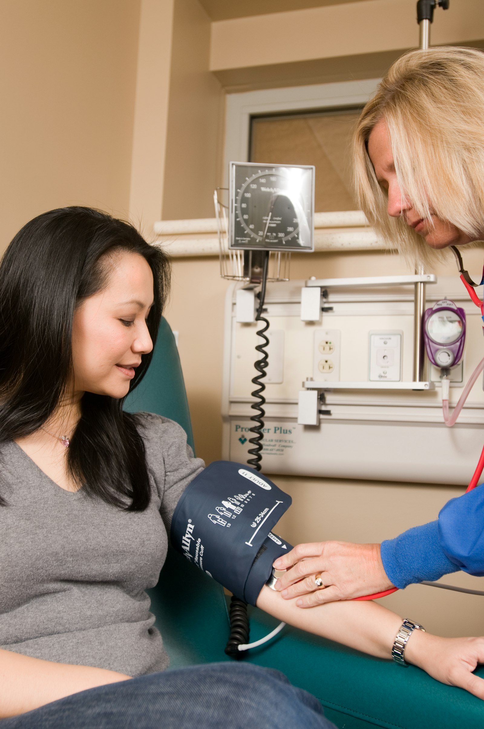 A doctor examining an Asian woman patient with a stethoscope