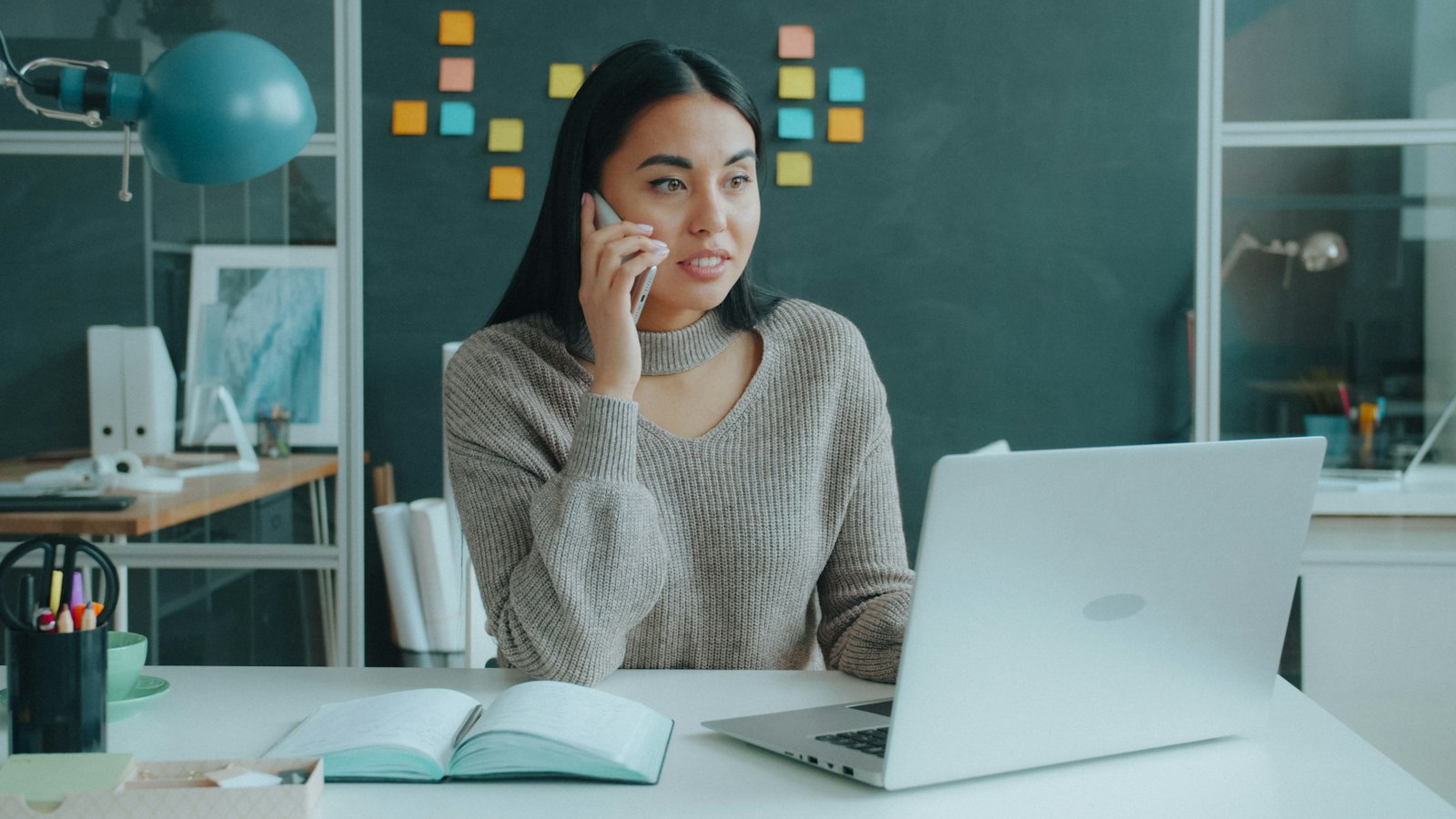 An Asian woman on the phone while working on a laptop